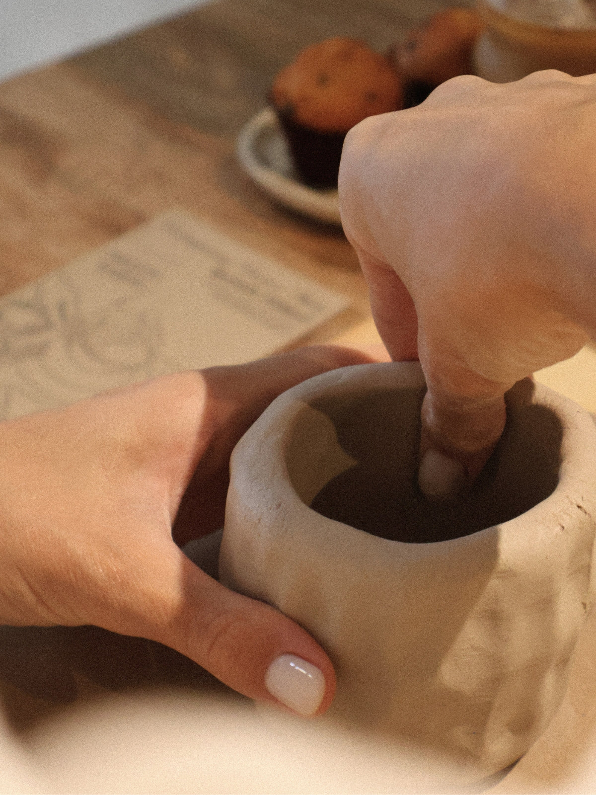 Close-up of hands shaping clay during a ceramic hand-building workshop in Dubai, with pastries in the background adding a warm studio atmosphere, from Maison Terraē.