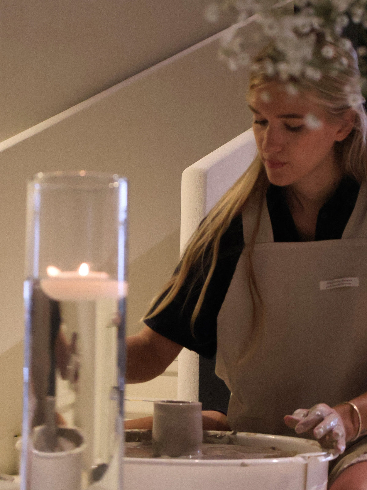 A participant shaping clay on the wheel during a ceramic workshop in Dubai, with a floating candle adding a calm studio atmosphere, from Maison Terraē.