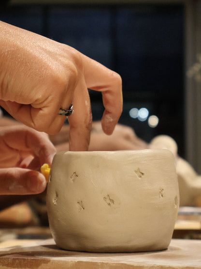 A participant adding small decorative stamps to a hand-built clay bowl during a ceramic hand-building workshop in Dubai, in the calm creative atmosphere of Maison Terraē.
